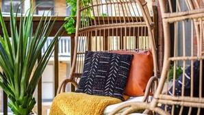 A wicker chair with cushions and a yellow throw blanket on a green artificial grass surface.