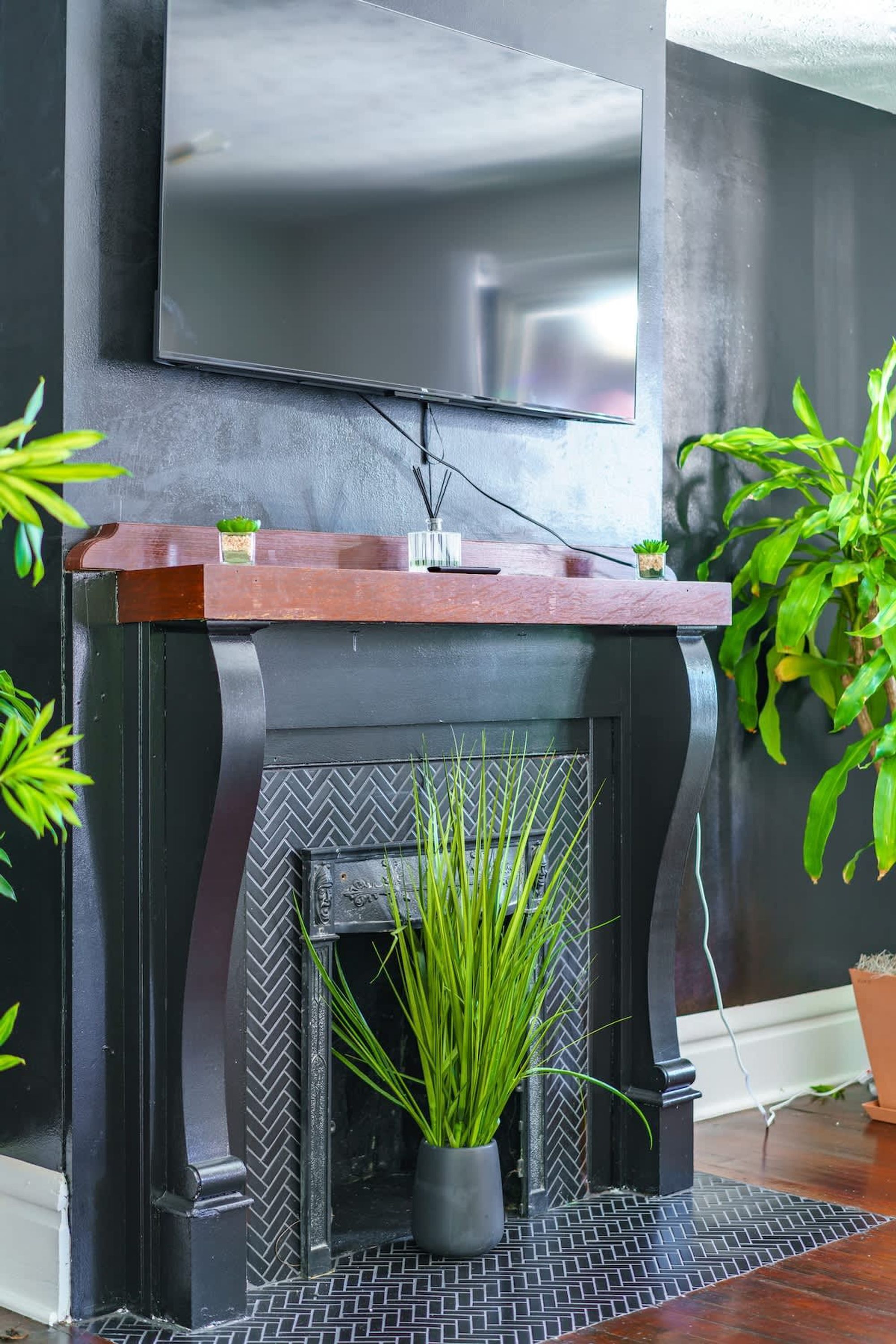 A modern fireplace with a wooden mantel, a television mounted above it, and a potted plant in front.