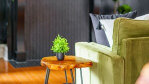 A modern living room with a green sofa, a small wooden stool with a plant, and a fireplace with a shelf above. - Prime Location Top Rated Clean Parking Free (Columbus)