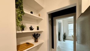 Un pasillo con paredes blancas, estantes de madera y una puerta enmarcada en negro que da a otra habitación.