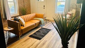 Una sala de estar con un sofá de cuero, una mesa de centro de madera, una alfombra negra y una planta grande.
