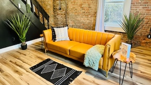 Una sala de estar moderna con un sofá amarillo, un tapete con estampado blanco y negro, y dos plantas en macetas.