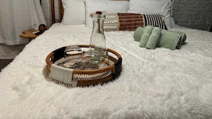A bed with a white fluffy cover, a woven basket with a glass bottle, and a wooden headboard. - Short North Convention King Bed Free Parking (Columbus)