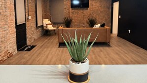A modern living room with a brick wall, a flat-screen TV mounted above a sofa, and a potted plant in the foreground. - Short North Convention King Bed Free Parking (Columbus)
