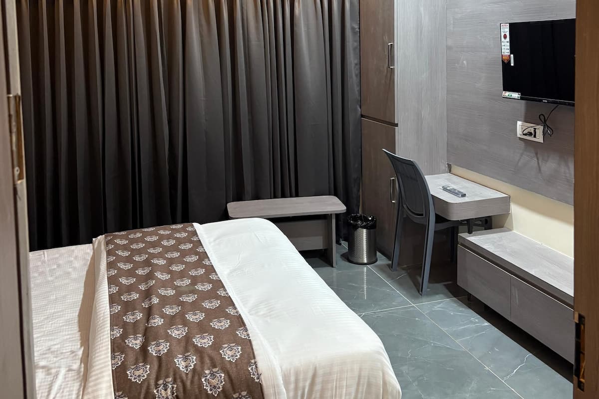 Una habitación de hotel con cama, escritorio, silla, televisor y ventilador de techo.