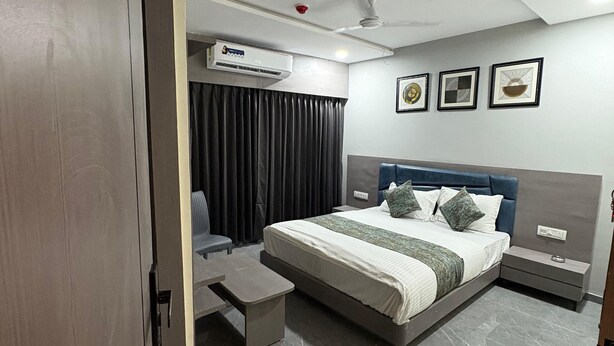 A modern hotel room with a large bed, a desk, a chair, and an air conditioning unit. - Hotel R Town (Vadodara)