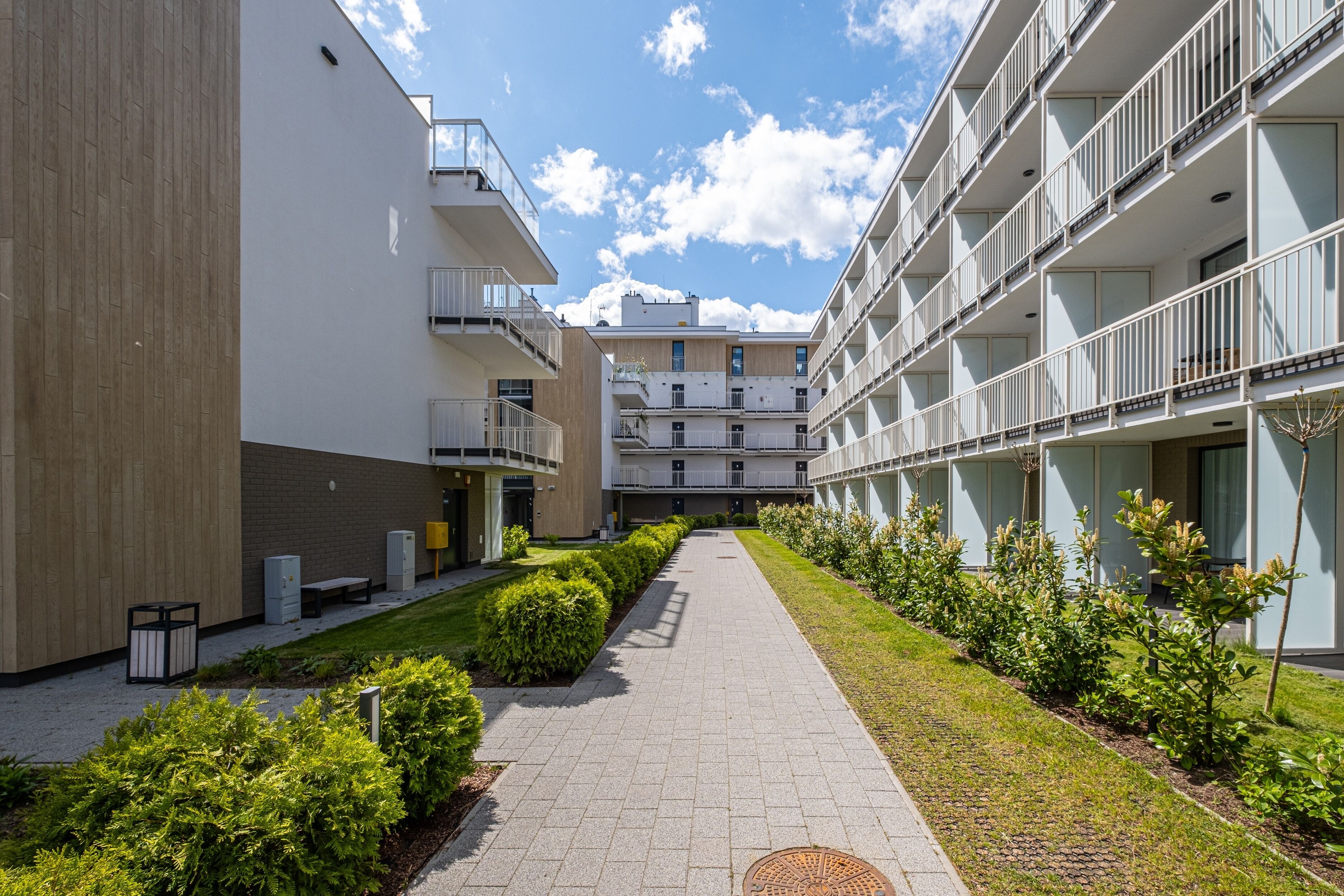 Un bâtiment moderne doté d’une cour intérieure, avec un chemin bordé de verdure et un banc.