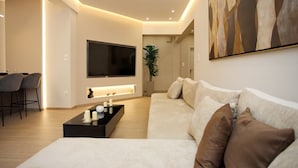 Een moderne woonkamer met een grote flatscreen televisie, een bank, een salontafel en een eethoek met stoelen.