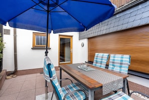 A patio with a table, chairs, and a blue umbrella.