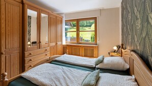 Ein Schlafzimmer mit zwei Betten, einem Holzschrank, einem Fenster mit Blick ins Grüne und einer Heizung.