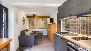 Eine kleine Küche mit eingebautem Herd, einer Holzausziehtafel und einem grauen Sofa im Wohnbereich.