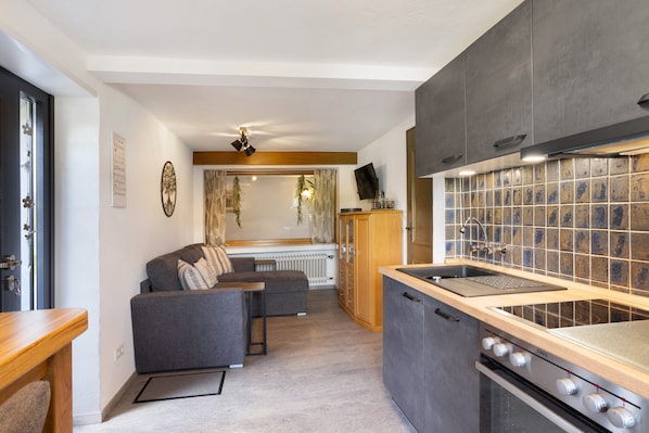 A compact kitchen with a built-in stove, a wooden countertop, and a grey sofa in the living area.