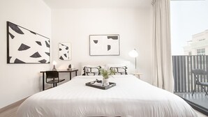A modern hotel room with a large bed, a desk, a chair, and a potted plant. - Hamilton House Studio: Rooftop Pool & Gym Access (Dubai)