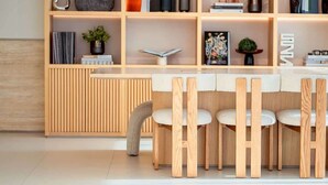 A modern interior with a wooden dining table and chairs, a bookshelf with various items, and a radiator. - Hamilton House Studio: Rooftop Pool & Gym Access (Dubai)