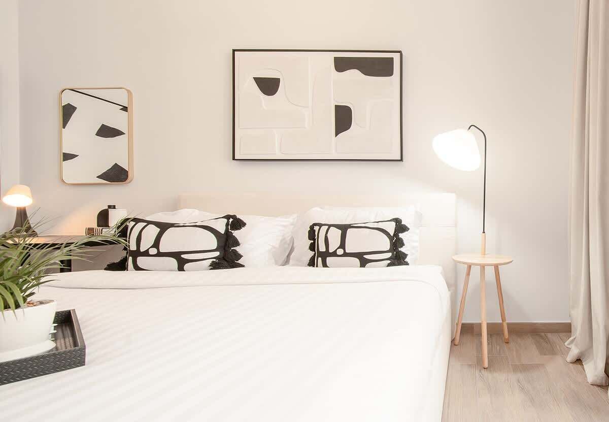 A modern bedroom with a bed, two abstract wall art pieces, a bedside lamp, and a small wooden side table.