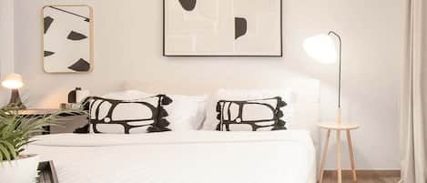 A modern bedroom with a bed, two abstract wall art pieces, a bedside lamp, and a small wooden side table.