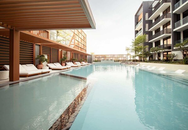 A modern hotel with a swimming pool, lounge chairs, and a covered seating area.