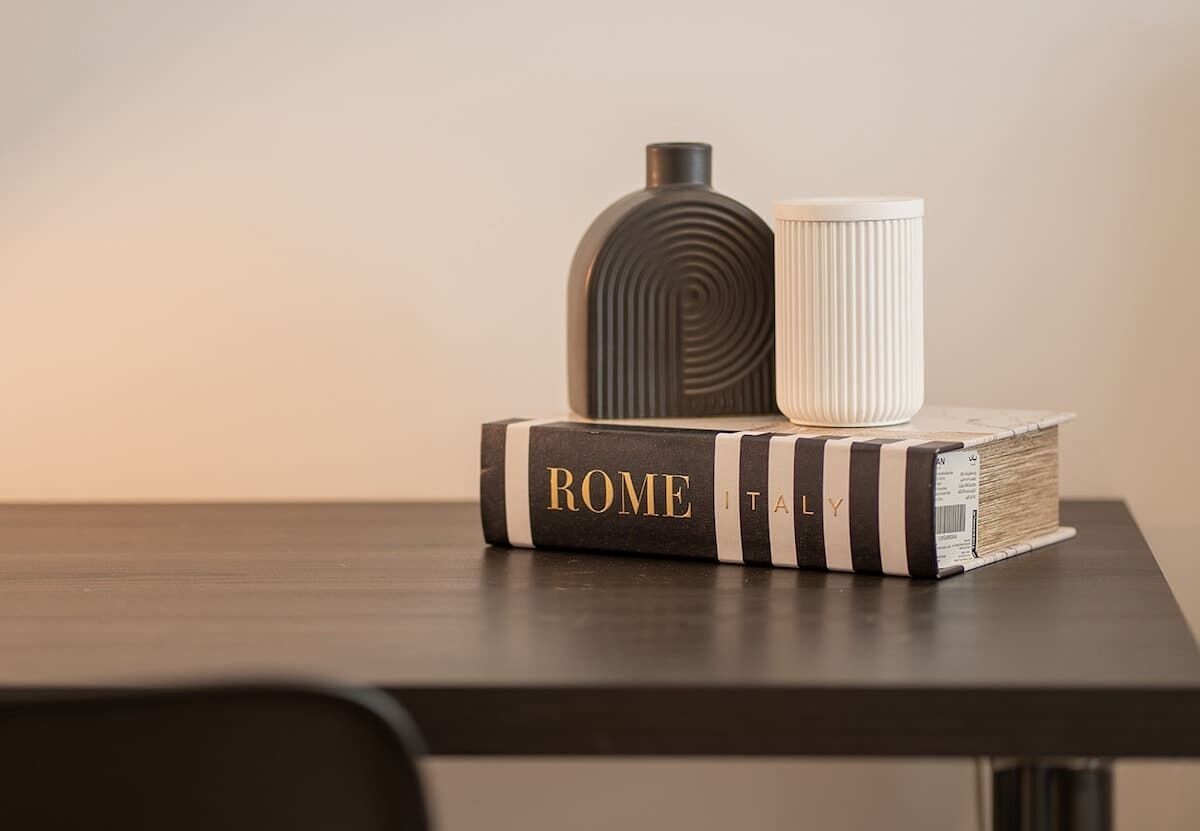 Un livre intitulé « ROME, ITALIE » est posé sur une table, accompagné d’un récipient cylindrique et d’un récipient à surface striée placés sur le dessus.