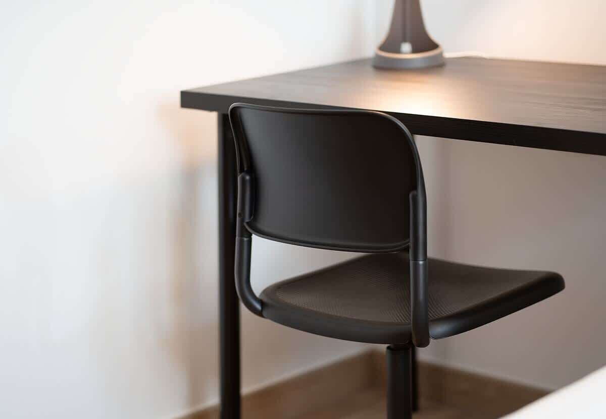 A modern chair with a high backrest and a cushioned seat, positioned at a corner of a room with a dark-colored table.