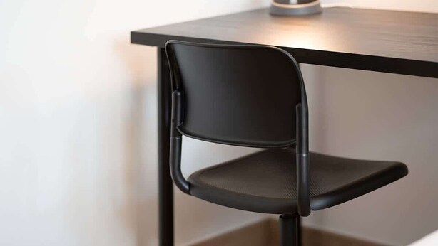 A modern chair with a high backrest and a cushioned seat, positioned at a corner of a room with a dark-colored table. - Hamilton House Studio: Rooftop Pool & Gym Access (Dubai)
