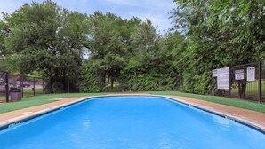 Une piscine rectangulaire à l’eau d’un bleu limpide, entourée d’une clôture métallique et de luxuriants arbres verdoyants.