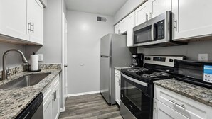 Una cocina moderna con gabinetes blancos, electrodomésticos de acero inoxidable, encimeras de granito y horno empotrado.