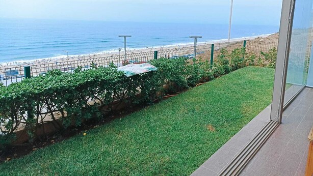 Une vue d’une plage avec une clôture et de la végétation au premier plan.