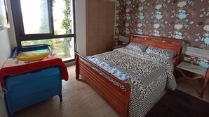 Une chambre à coucher comprenant un lit, un petit bureau, une chaise, une armoire et une fenêtre donnant sur un paysage verdoyant.