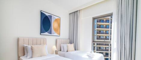 Hotellihuone, jossa on kaksi sänkyä, suuri ikkuna, jossa on verhot, ja näkymä kaupunkiin.