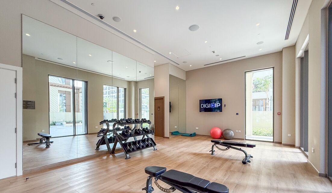 A modern gym with exercise equipment, large mirrors, and a TV screen.