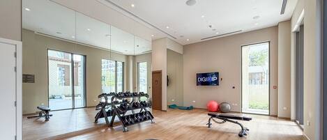 A modern gym with exercise equipment, large mirrors, and a TV screen.
