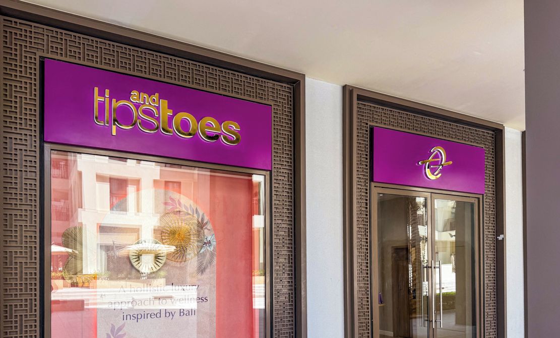 Ein Schaufenster mit einem violetten Schild mit der Aufschrift 'and tips tooes' und einem weiteren Schild mit einem stilisierten 'Q'.