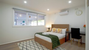Ein Schlafzimmer mit Bett, Nachttisch, Stuhl, Schreibtisch und einem Fenster.