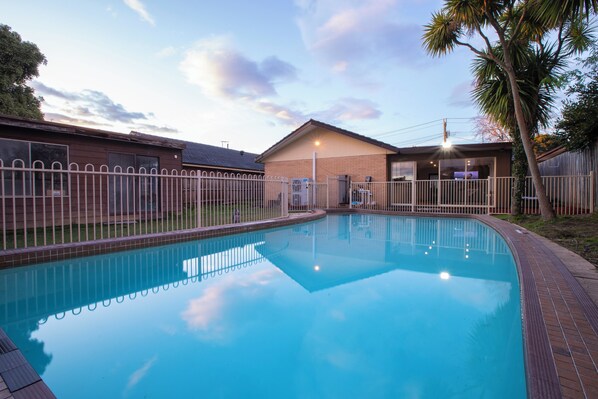 A swimming pool with a fenced area, a building with a brick facade, and a palm tree. - Pool, Games & fun - Family Retreat! (Boronia)
