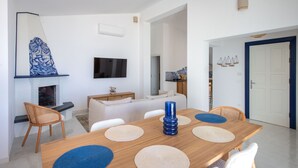 A modern living room with a wooden dining table, white sofas, and a fireplace.