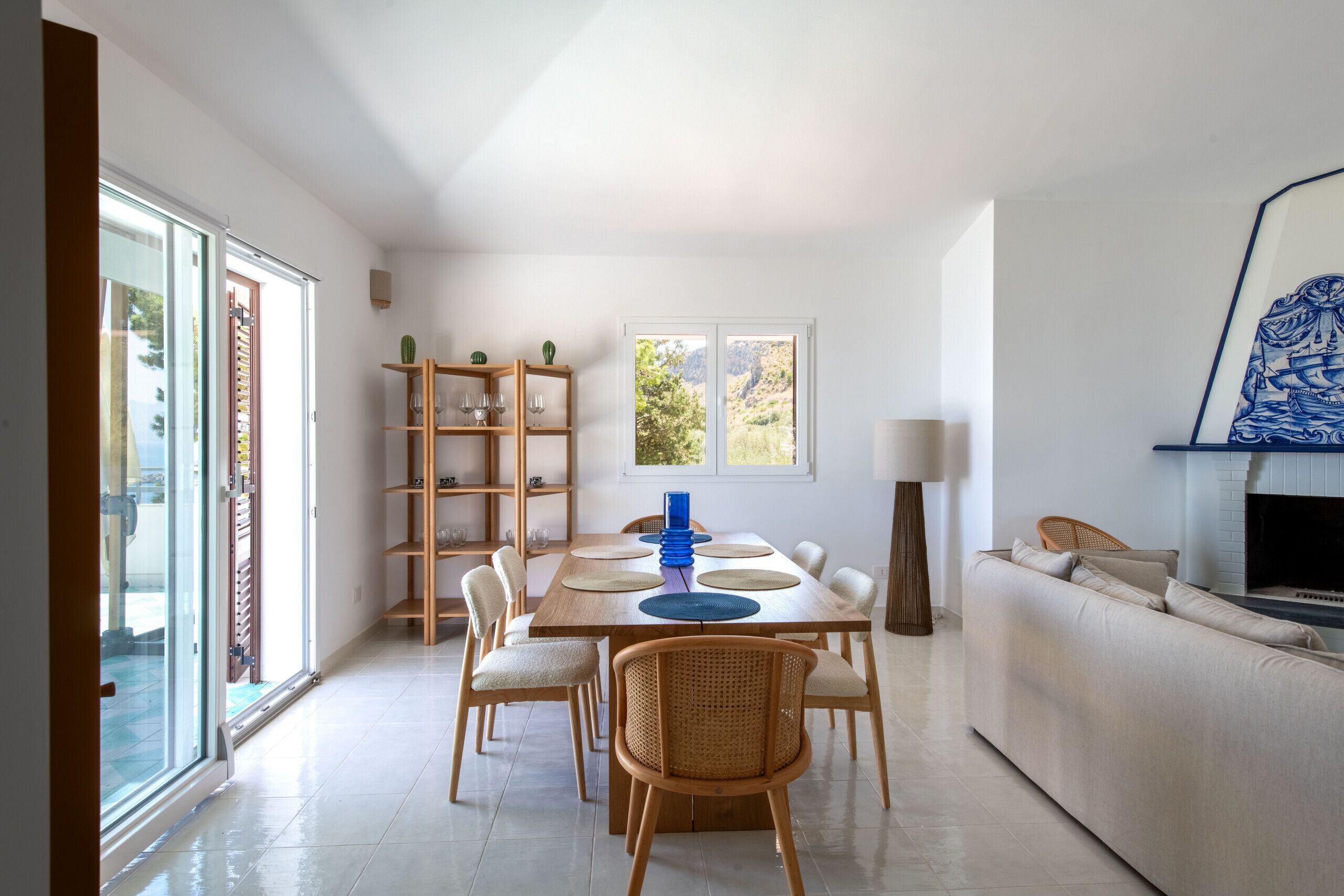 Ein modernes Wohnzimmer mit Essbereich, ausgestattet mit einer Couch, einem Fernseher, einem Kamin und einem großen Fenster mit Blick ins Freie.