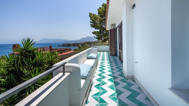 Ein Balkon mit Blick auf das Meer und die Berge, ein Fliesenboden und eine weiße Wand mit einem Fenster.