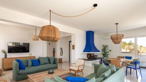 Ein geräumiges Wohnzimmer mit einem grünen Sofa, einem Holztisch und hängenden Lampen aus Weidengeflecht.