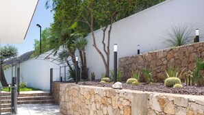 Eine steinerne Stützmauer mit Kakteengarten, Metallgeländern und einem weißen Gebäude mit geneigtem Dach.
