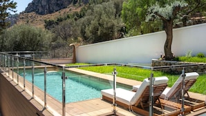 Ein Schwimmbecken mit Liegestühlen, umgeben von einer Holzterrasse und einer weißen Mauer.