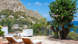 A patio with two wooden lounge chairs and a white cabinet, overlooking a rocky hillside and the sea. - Casa Solunto Vista Mare by Wonderful Italy (Santa Flavia)