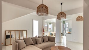 A modern living room with a large L-shaped sofa, a round wooden coffee table, and two woven pendant lights. - Casa Solunto Vista Mare by Wonderful Italy (Santa Flavia)