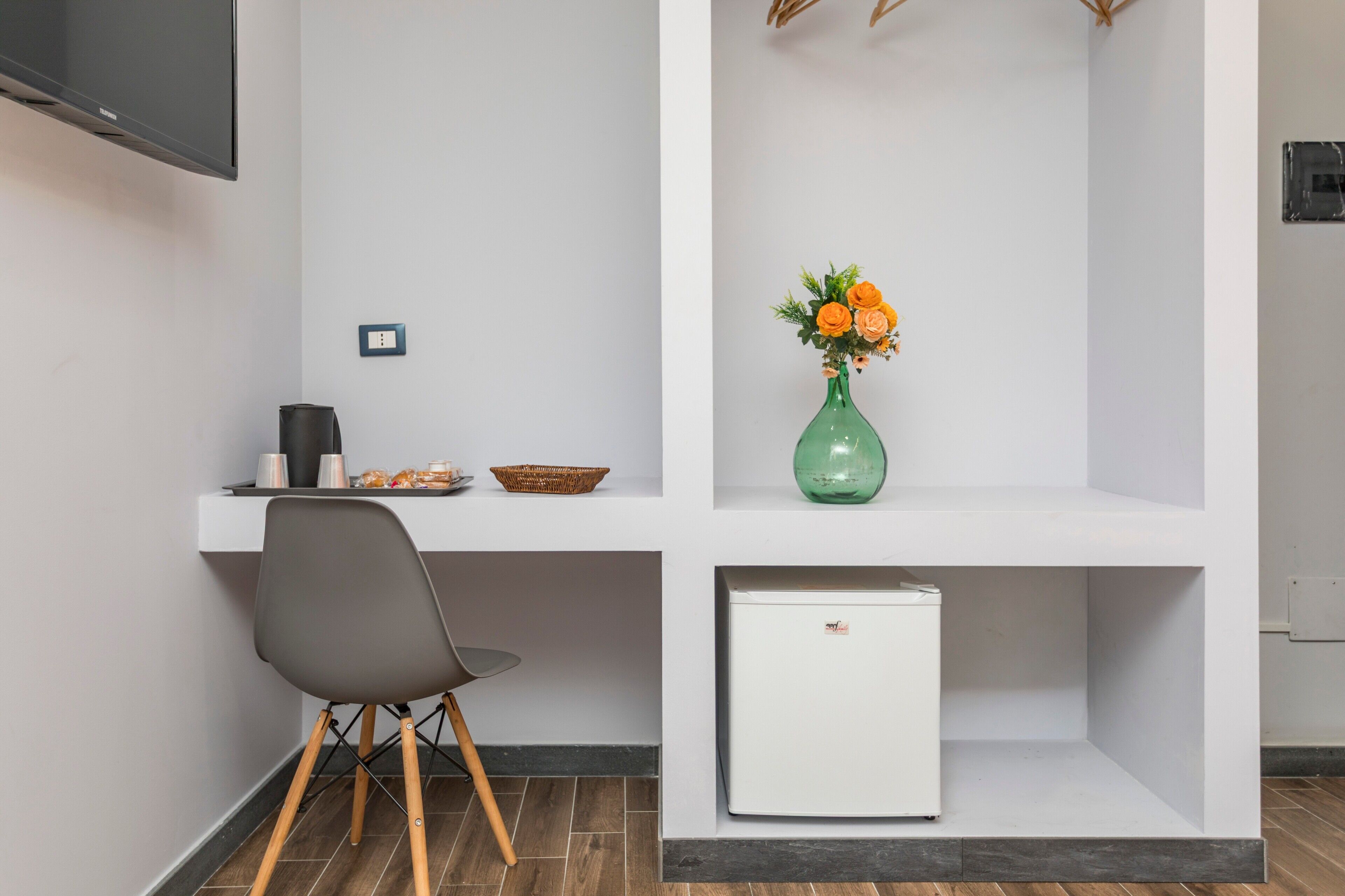 Eine moderne Küche mit weißer Arbeitsplatte, einem grünen Blumenvasen, einem weißen Kühlschrank und einem grauen Stuhl.