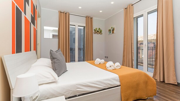 Ein modernes Schlafzimmer mit Bett, Kissen, einer Nachttischlampe, einem Fenster und Vorhängen.