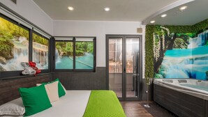 A bedroom with a bed, green pillows, a green blanket, a hot tub, and a mural of a waterfall.