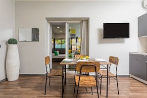 A dining area with a table set for four, a large potted plant, a flat-screen TV, and a sliding glass door leading to a balcony.