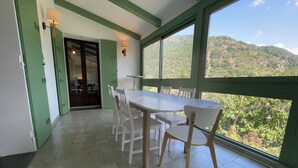 A dining area with a large table and chairs, green walls, and a view of a mountainous landscape through large windows. - Flowery villa: family home, veranda and garden (Tende)