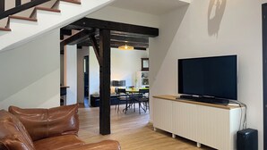 A living room with a brown leather sofa, a TV on a white stand, wooden flooring, and a staircase with wooden railings. - Flowery villa: family home, veranda and garden (Tende)
