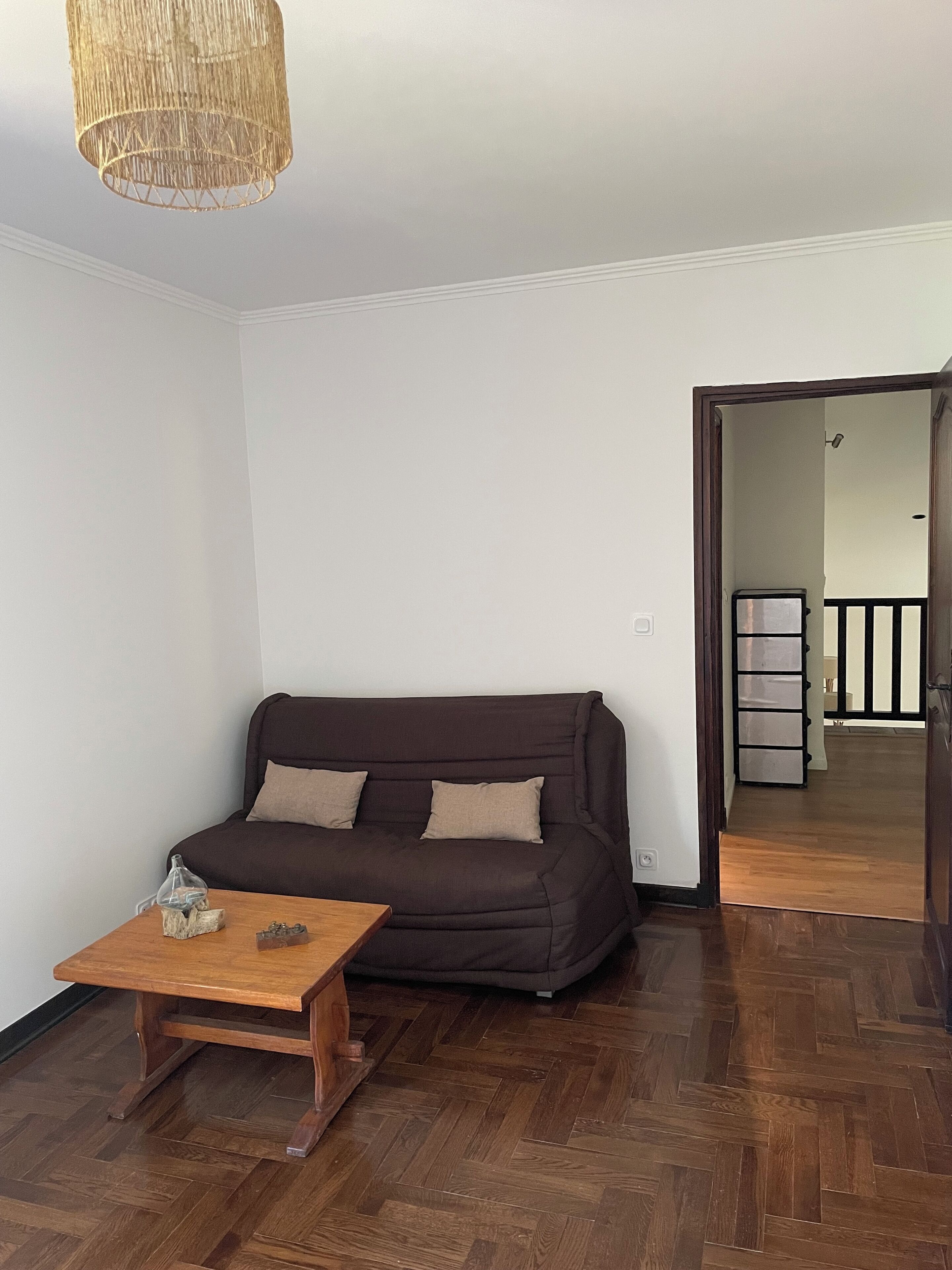A living room with a dark brown sofa, a wooden coffee table, and a woven pendant light.