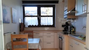 Une cuisine équipée d’une table à manger, de chaises, de placards, d’une fenêtre avec des rideaux et offrant une vue sur l’extérieur.